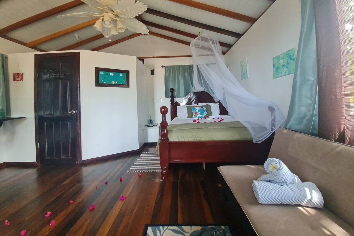 Un dormitorio con una cama bajo un dosel, techo de madera, un sofá y una pequeña mesa con una lámpara.