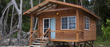 A wooden cabin with a porch and a staircase, surrounded by trees.