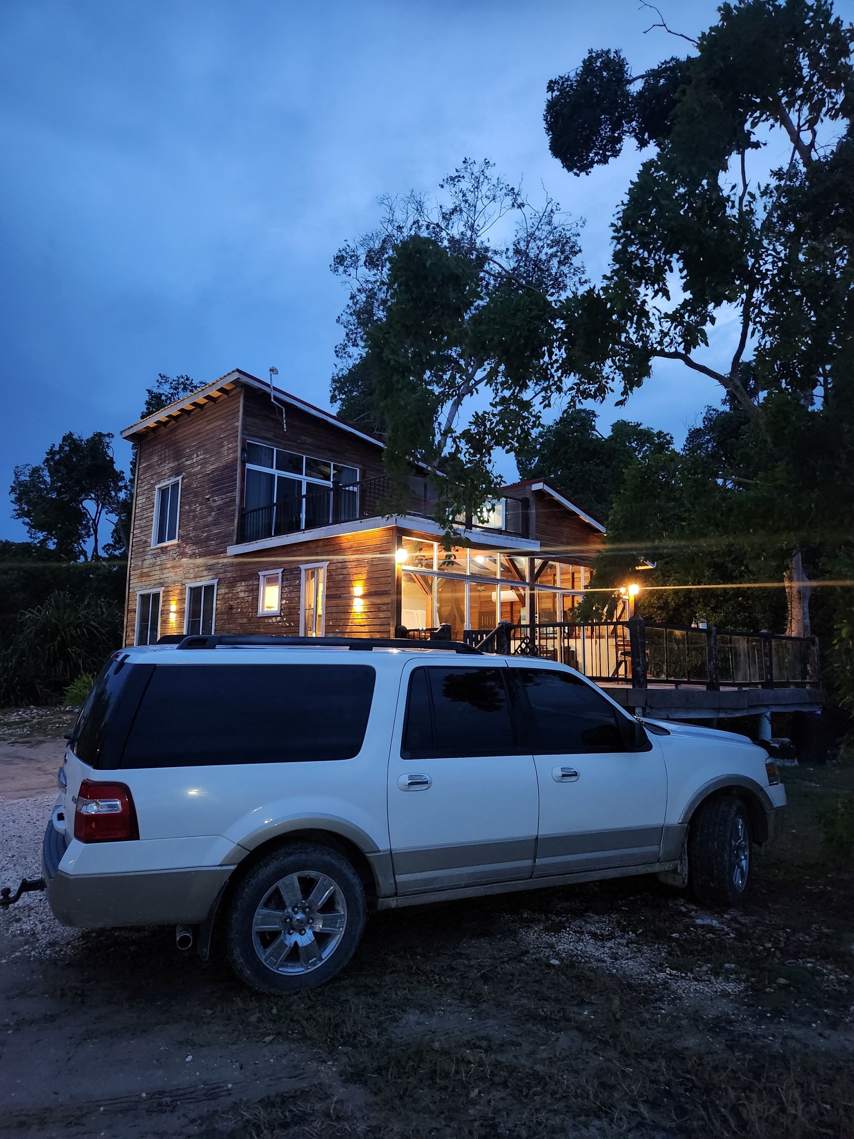 Un SUV blanco estacionado frente a una casa de dos pisos con balcón y terraza.