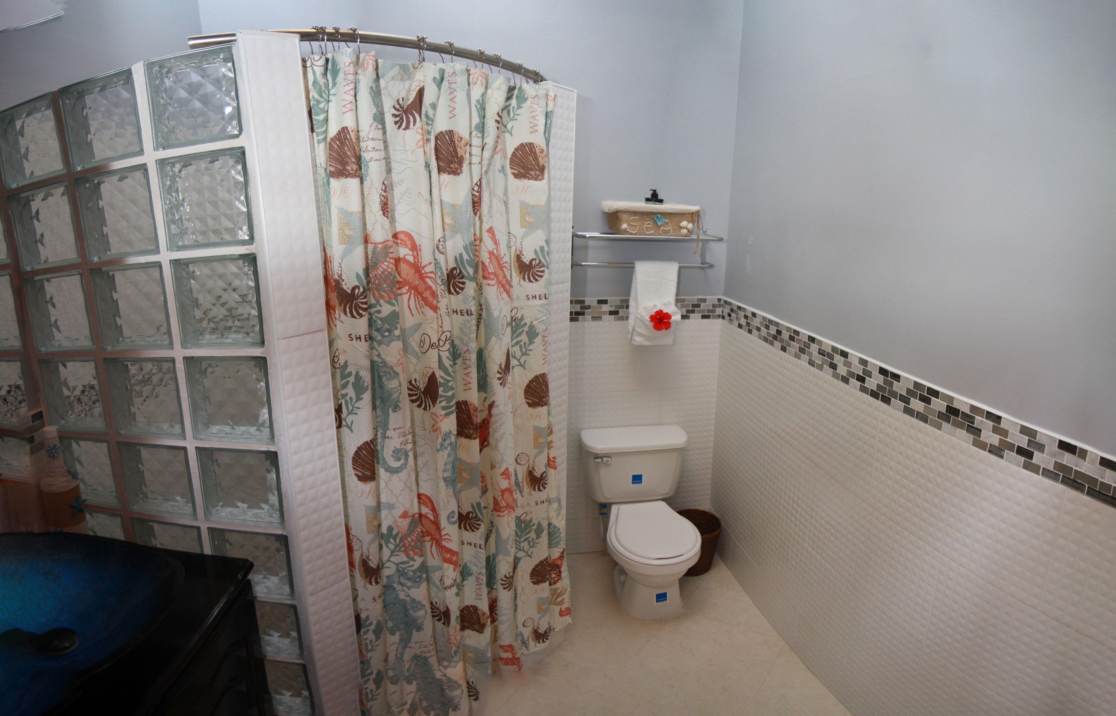 Een badkamer met toilet, een plankje met toiletartikelen en een douchegordijn met een bloemenprint.
