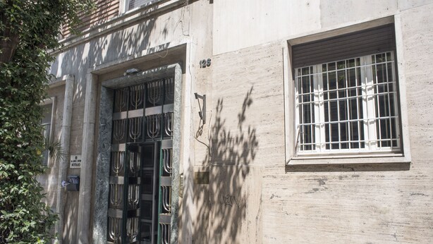 Fachada de edificio con un grande portón metálico, una ventana con rejas de seguridad y un letrero que indica una notaría.