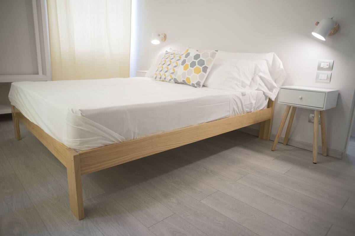 A single bed with a wooden frame, white bedding, and a bedside table with a lamp.