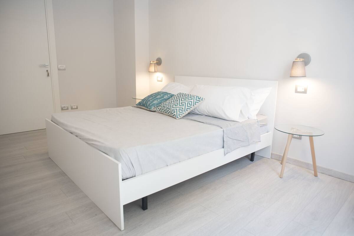 A modern bedroom with a white bed, patterned pillows, and bedside lamps.