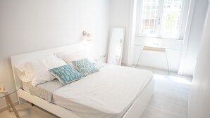 Una cama blanca con almohadas estampadas, una mesita de noche y un espejo.