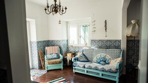 Un salón con un sofá azul, un sillón estampado y una araña.