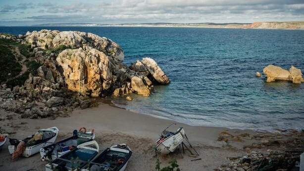 Una costa rocosa con barcos en la orilla y una vista despejada del mar.