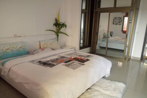 A bedroom with a bed, a white rug, a potted plant, and a sliding glass door leading to another room. - Residences Est 2 T3 (Abidjan)