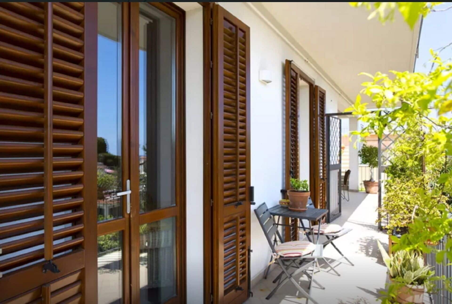 A balcony with wooden shutters, a table with chairs, and potted plants.