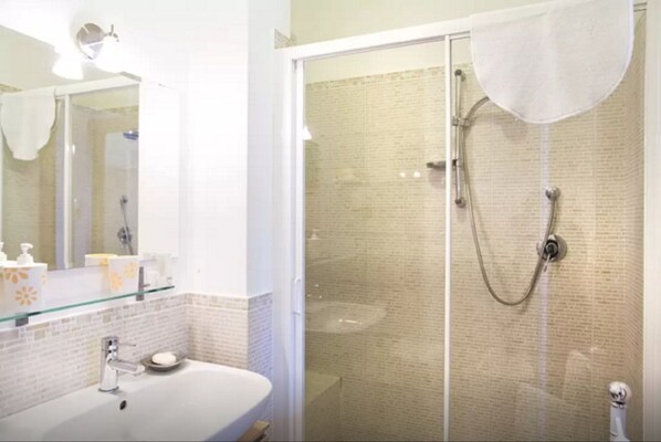Une salle de bain avec une douche à parois de verre, un lavabo doté d’un distributeur de savon et un miroir au-dessus du lavabo.