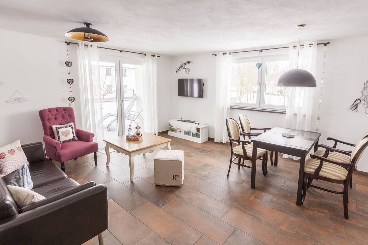 A modern living room with a sofa, armchair, dining table, and chairs.