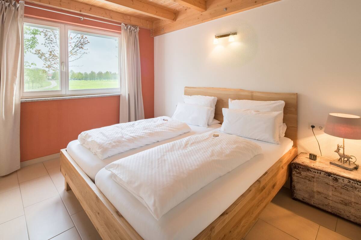 A double bed with white linens, a wooden headboard, and a bedside table with a lamp.