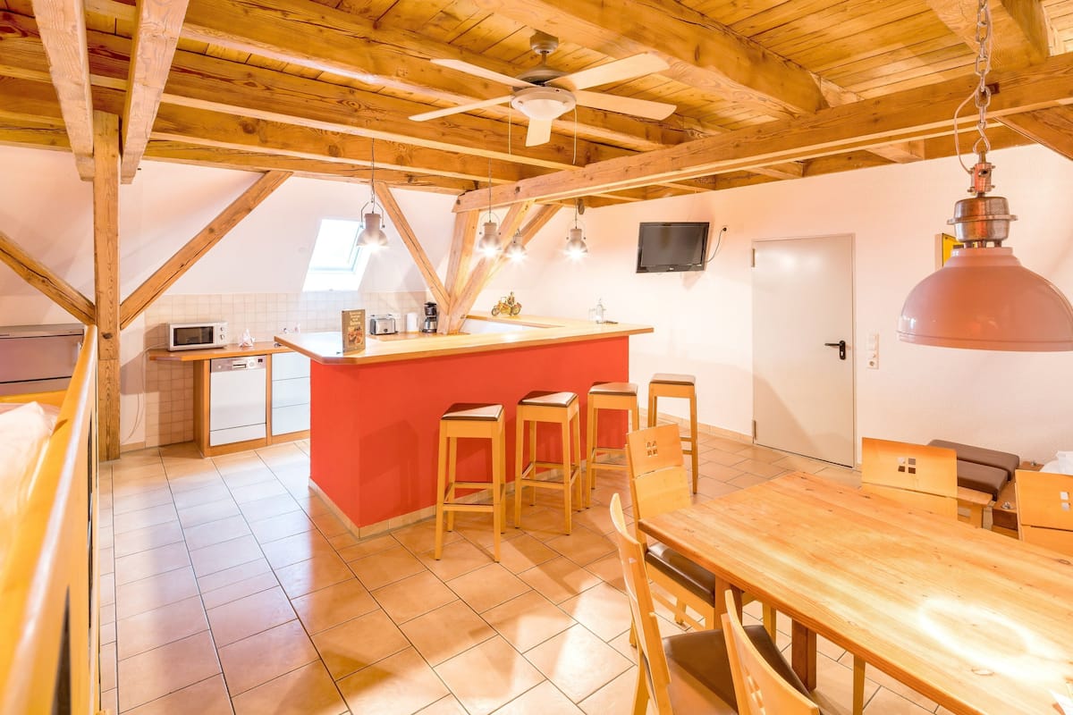 A kitchen with a red island, wooden stools, a wooden dining table, and a ceiling fan.