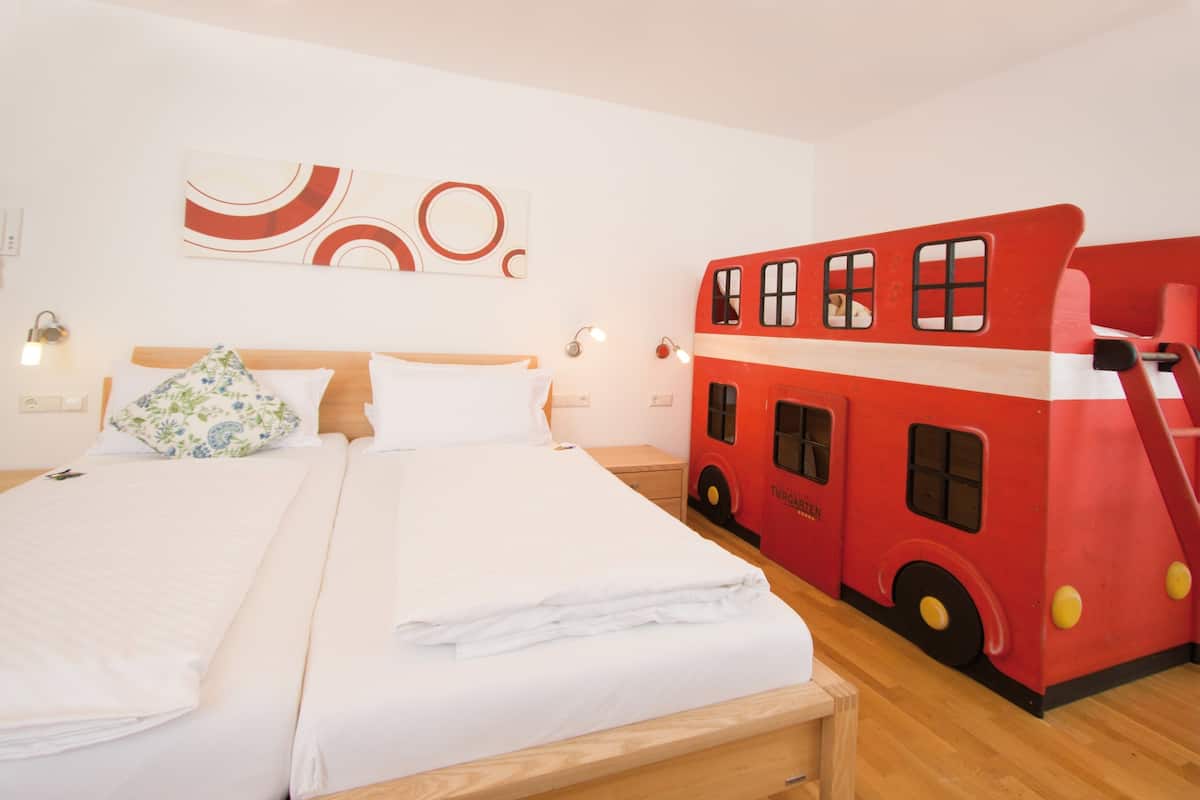 A double bed with white linens, a wooden headboard, and a floral pillow. There is a red double-decker bus-shaped wall decoration.