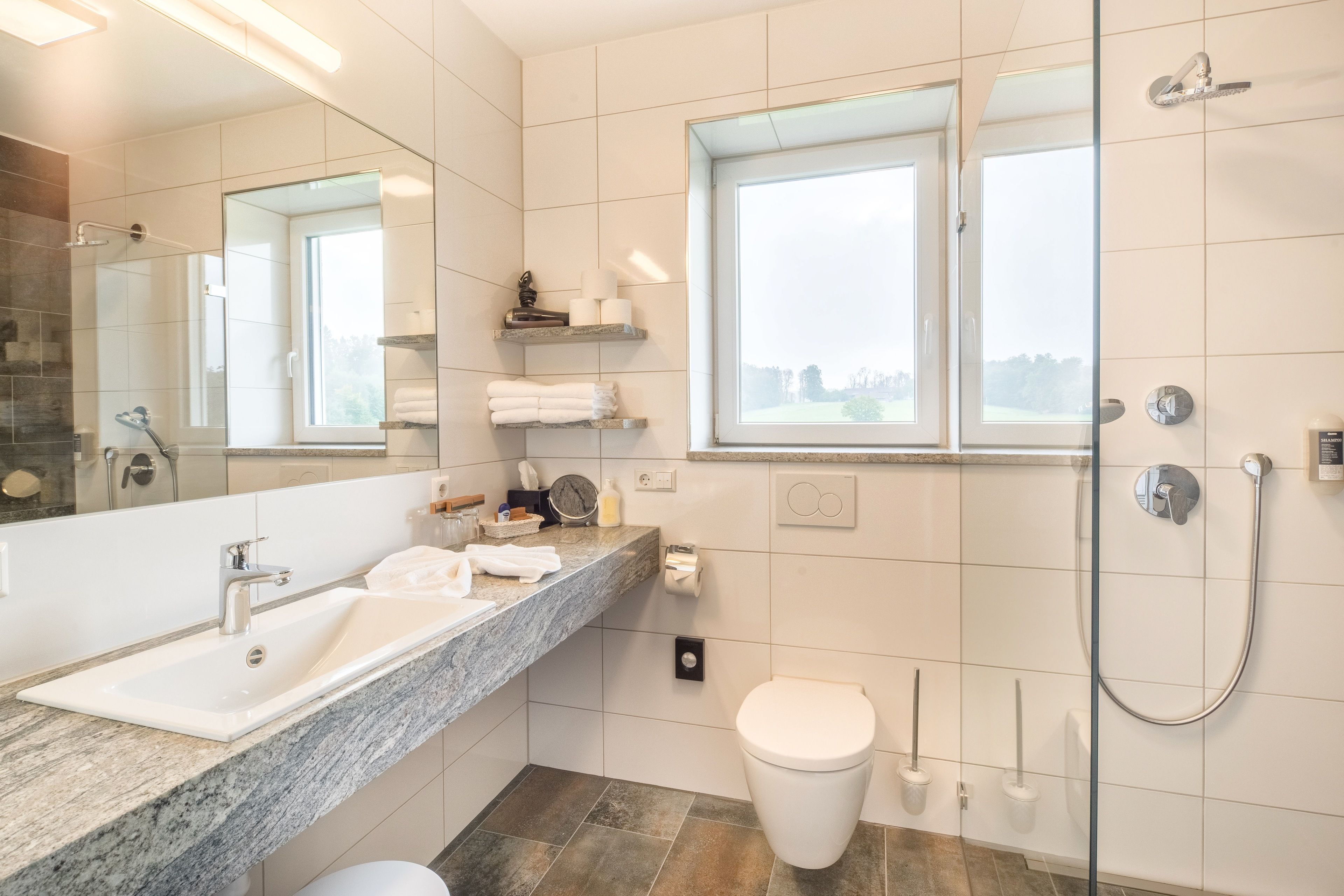 Un baño moderno con un espejo grande, un lavabo, un inodoro y una ducha.