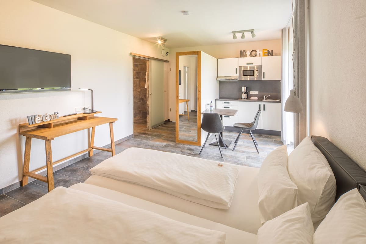 A hotel room with a bed, a desk, a chair, and a kitchenette.