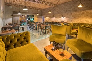 A modern interior with a mix of seating areas, including a green sofa and chairs, and a bar area with stools. - Hotel Hofgut Tiergarten (Aulendorf)