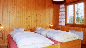 A wooden cabin bedroom with two beds, a hanging light fixture, and a window with curtains.