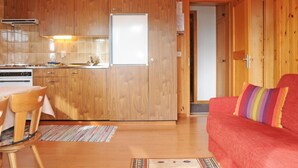 A compact wooden cabin with a kitchenette, a dining area, and a living room with a red sofa.