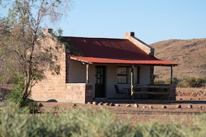 A stone building with a red roof, a porch with chairs, and a clear view of the surrounding landscape.