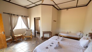 Una habitación de hotel con dos camas, una silla de madera, una mesita pequeña y un rincón con ducha.