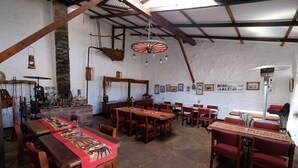 Un comedor rústico con mesas y sillas de madera, suelo de piedra y un techo alto con vigas a la vista.