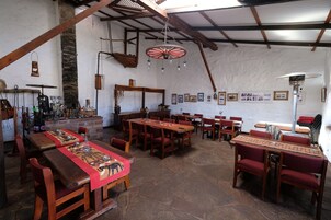Un comedor rústico con mesas y sillas de madera, suelo de piedra y un techo alto con vigas a la vista.