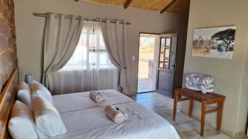 Quarto com duas camas, cabeceira de madeira, uma mesinha e porta que dá para o exterior.