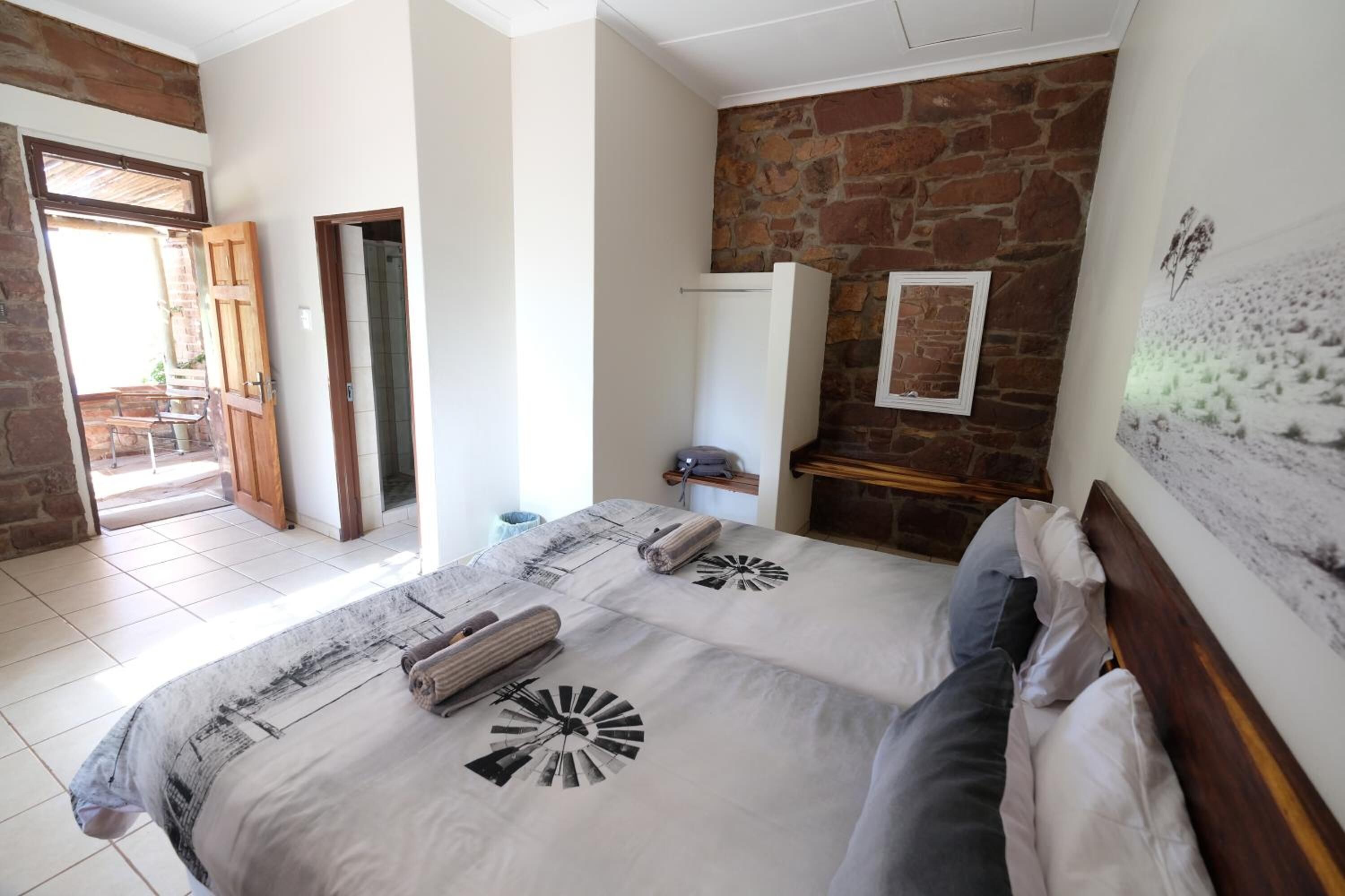Une chambre à coucher avec un grand lit, une tête de lit en bois, un mur en pierre et une porte donnant sur un balcon.