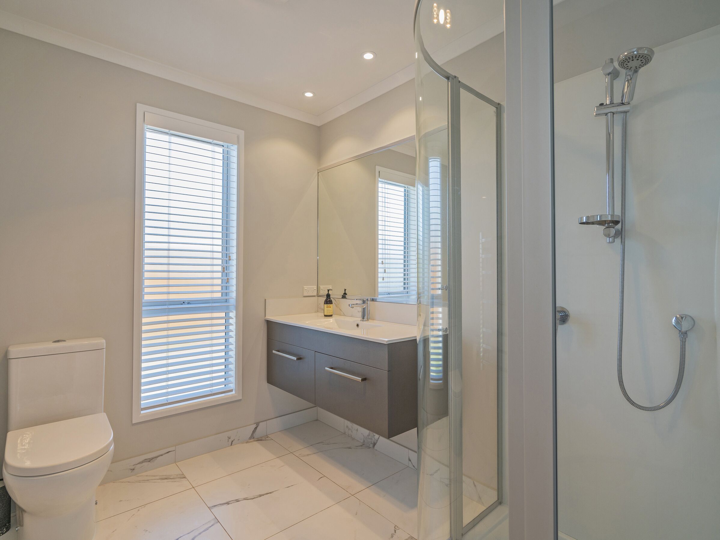 Une salle de bain moderne comprenant des toilettes, un meuble-lavabo avec un miroir et une douche séparée par des parois en verre.