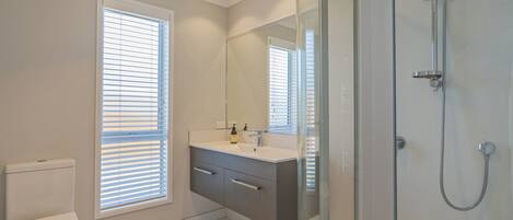 Une salle de bain moderne comprenant des toilettes, un meuble-lavabo avec un miroir et une douche séparée par des parois en verre.