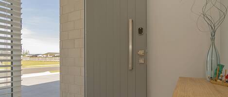 A modern entryway with a grey door, a small window with blinds, and a wooden table with a vase.