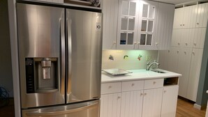 Una cocina moderna con refrigerador de acero inoxidable, gabinetes blancos, un lavamanos empotrado y piso de madera.