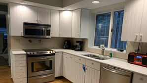 Una cocina moderna con armarios blancos, electrodomésticos de acero inoxidable y un ventanal que proporciona luz natural.