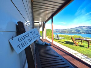 A sign reading "GONE TO THE BEACH" on a wooden bench with a view of a beach and mountains. - Hector's Tiny House - Akaroa Holiday Home (Duvauclle,Robinson's Bay)
