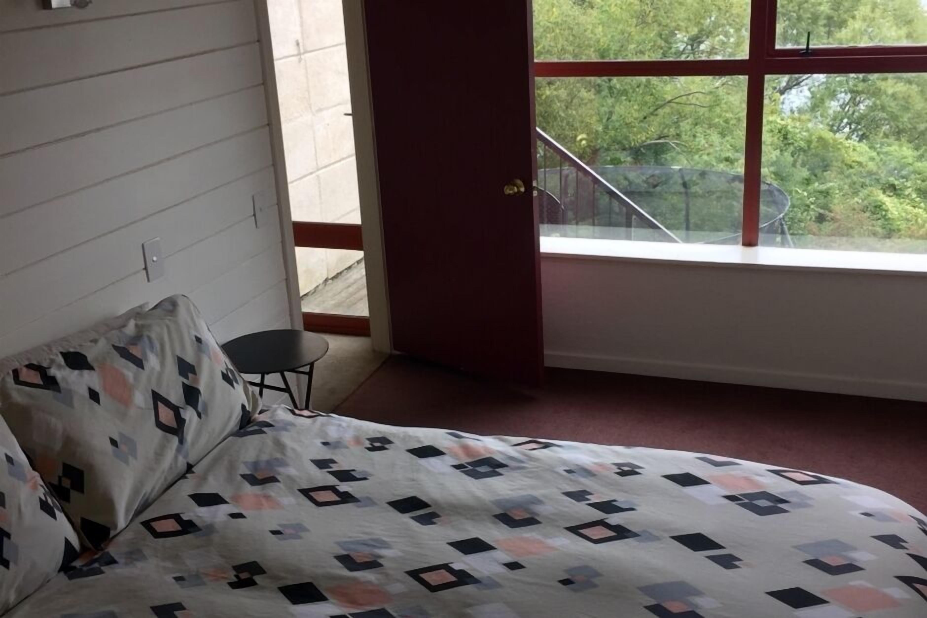 A bedroom with a bed, a chair, and a window with a view of trees.