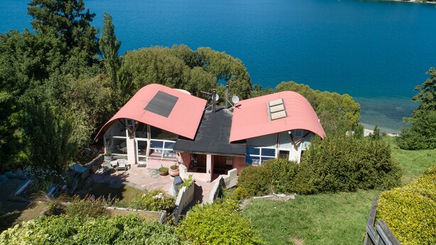 A house with a red roof, surrounded by lush greenery and a lake. - Lakes Edge Apartment - Unit A (Queenstown)