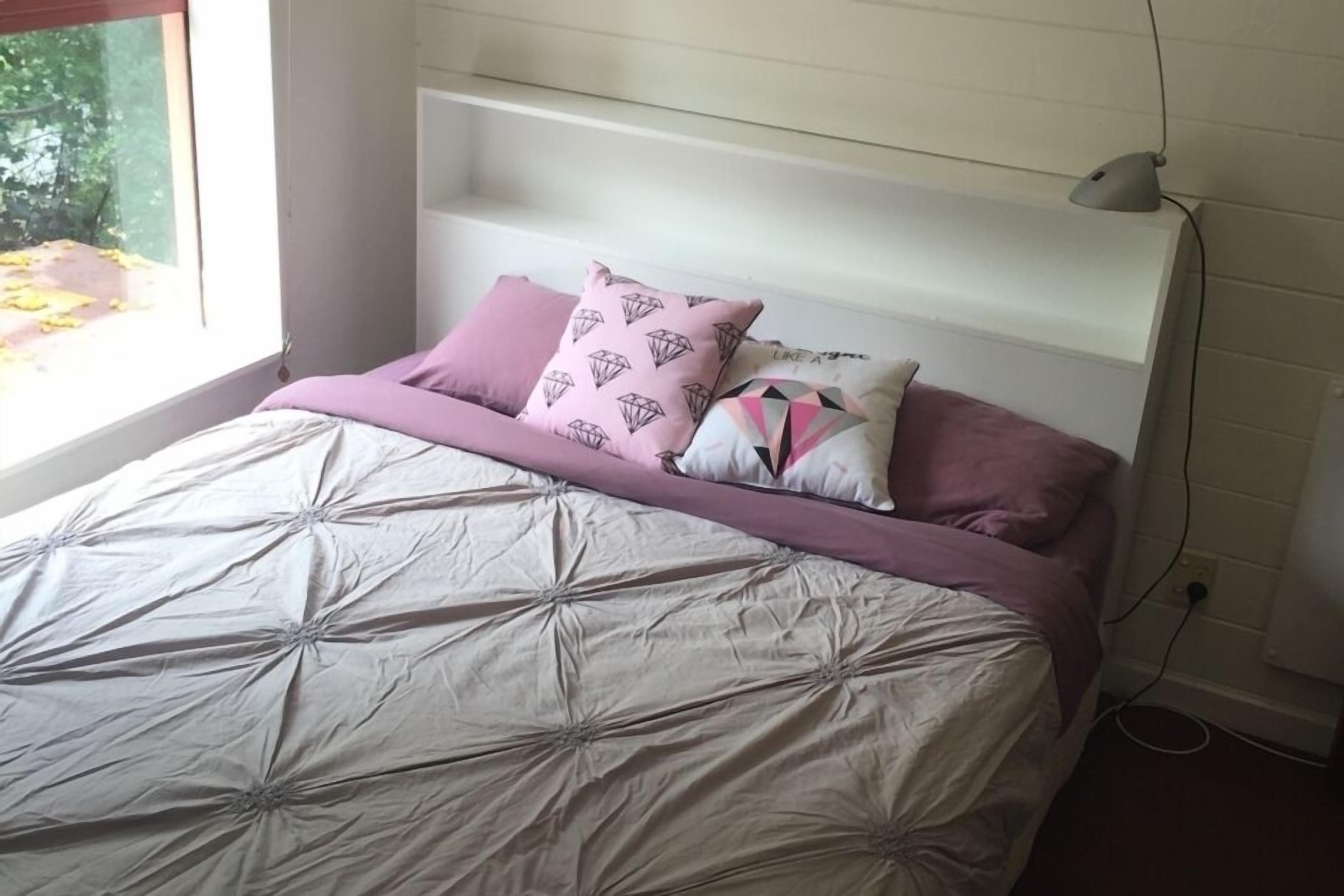 A bed with a patterned bedspread, a headboard, and three pillows with different designs.