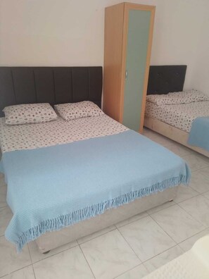 A room with two beds, a wardrobe, and a tiled floor.