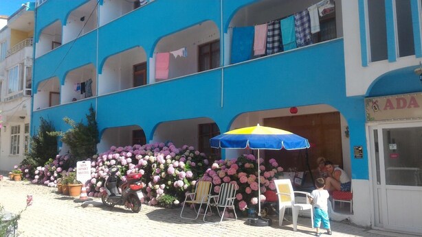Un edificio azul con balcones, un letrero que indica ADA apart motel, área de estar exterior con mesa y sillas, y una scooter estacionada al frente.