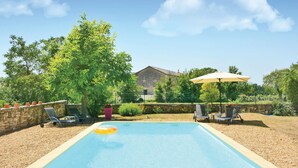 Ein Schwimmbecken mit Liegestühlen und einem Sonnenschirm, umgeben von Bäumen und einer Steinmauer.