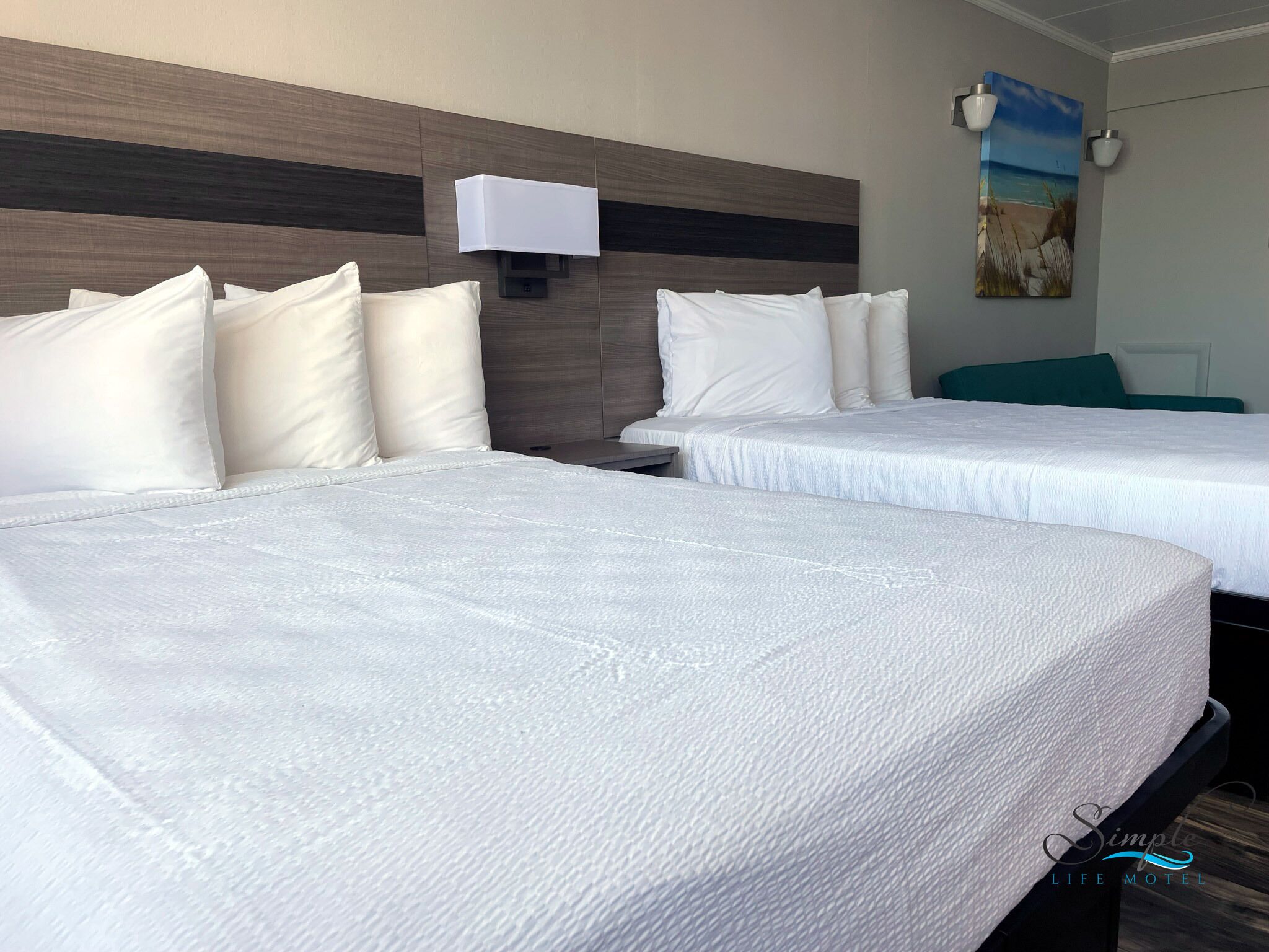 Een hotelkamer met twee bedden, een hoofdeinde met een lamp en een schilderij aan de muur.