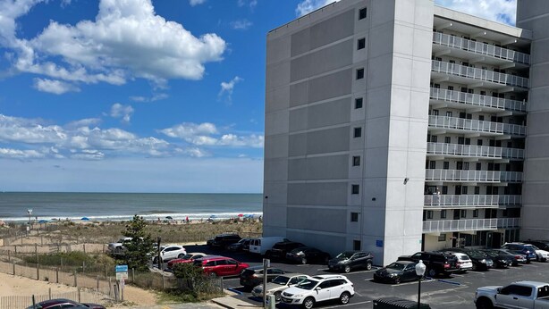 Ein mehrstöckiges Gebäude mit Parkplatz vor der Tür, mit Blick auf einen Strand.