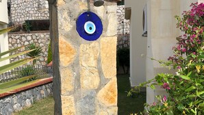Eine steinerne Säule mit blauer, augenähnlicher Verzierung, einem Klingelknopf aus Metall und einem kleinen Fenster.