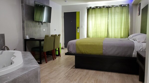 Hotellihuone, jossa on sänky, työpöytä, tuoli, televisio ja kylpyhuone, jossa on kylpyamme.
