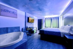 Moderni hotellihuone, jossa on suuri sänky, työpöytä, taulutelevisio ja kylpyamme.