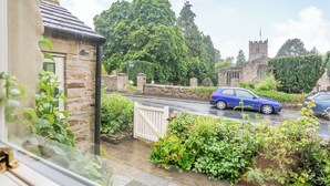 A residential street with a stone house, a blue car, and a church in the background. - 3 bedroom accommodation in Grinton, near Reeth (Grinton, near Reeth)