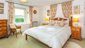 A neatly arranged bedroom with a large bed, two bedside tables with lamps, a chair, and a window with curtains. - 3 bedroom accommodation in Grinton, near Reeth (Grinton, near Reeth)