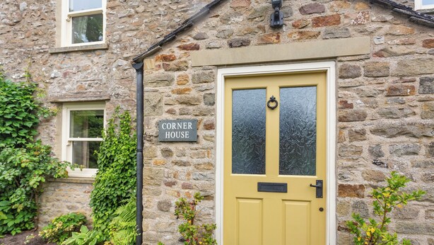 A stone house with a yellow door, a 'Corner House' sign, and potted plants around the entrance. - 3 bedroom accommodation in Grinton, near Reeth (Grinton, near Reeth)