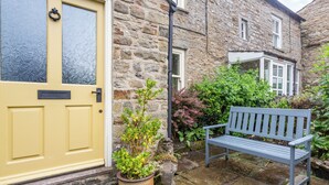A stone building with a yellow door, a bench, and potted plants. - 3 bedroom accommodation in Grinton, near Reeth (Grinton, near Reeth)