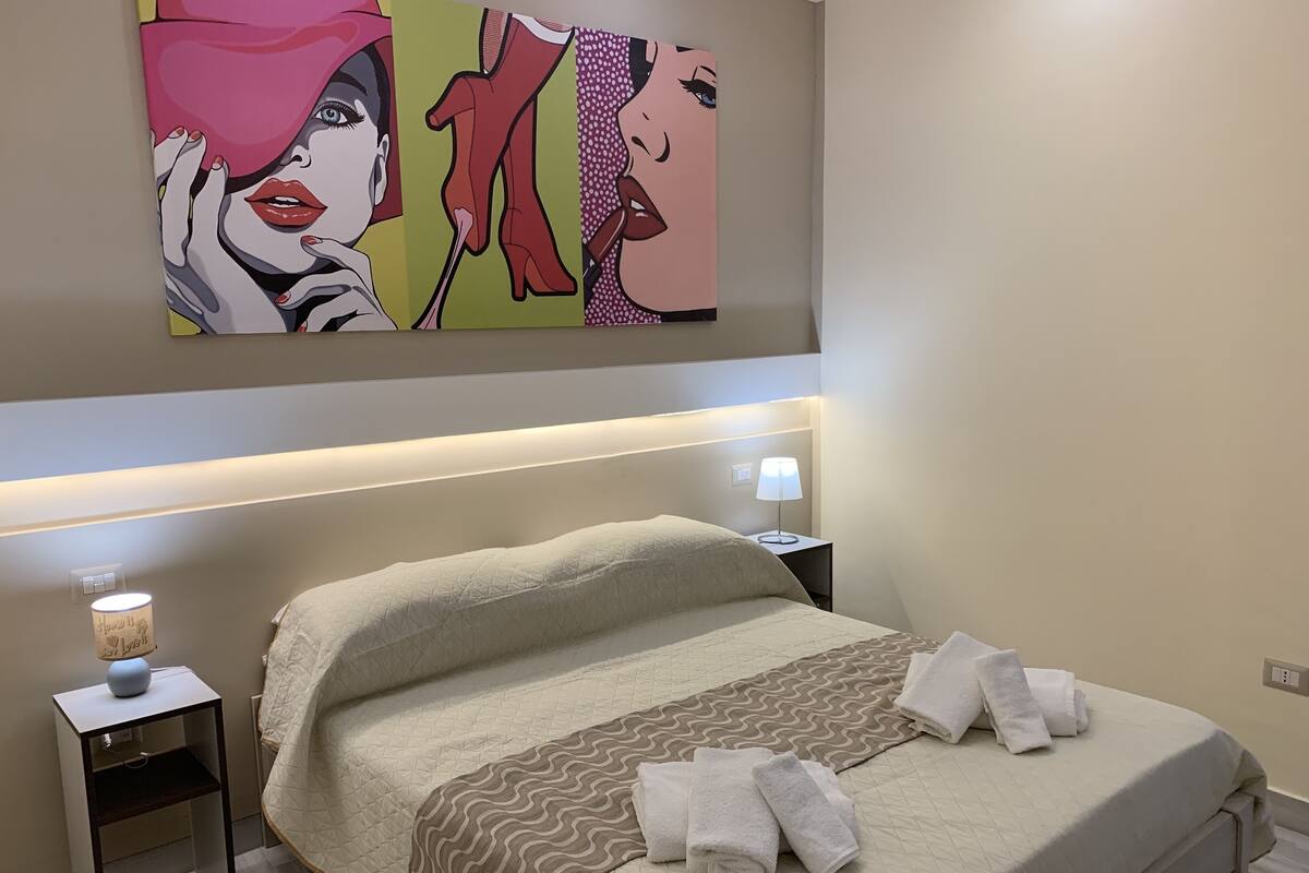 A neatly made bed with a quilted cover, two bedside lamps, and a wall-mounted painting.